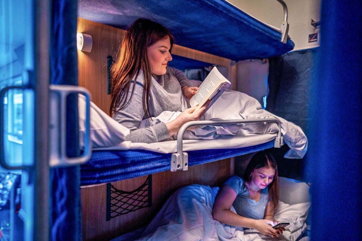 Two passengers in bunk beds on a sleeper train, reading and relaxing in their compartment