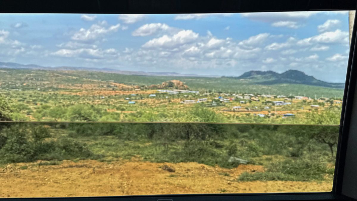Expansive Kenyan savanna landscape with scattered settlements and mountains under cloudy sky