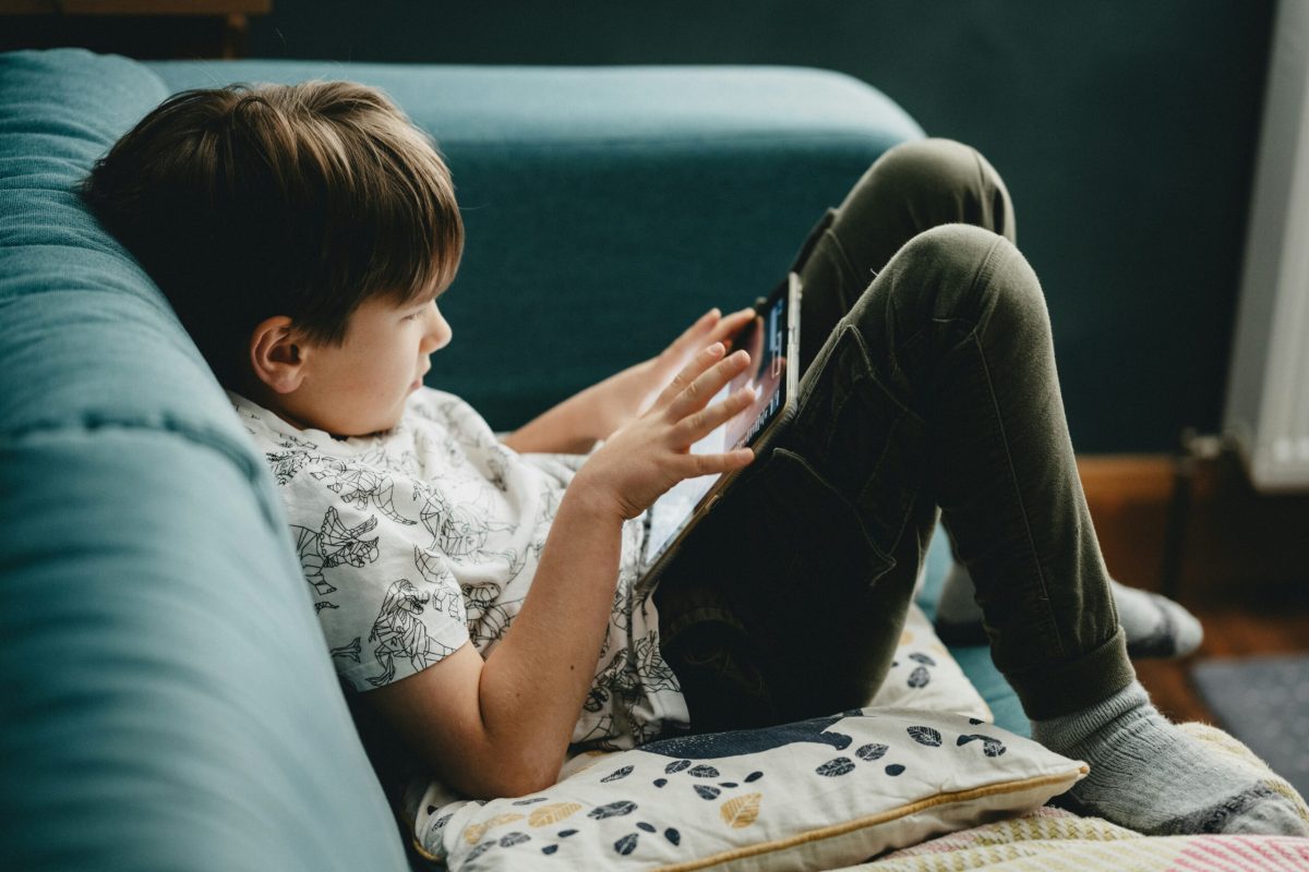 Young boy using smartphone while sitting on a teal couch