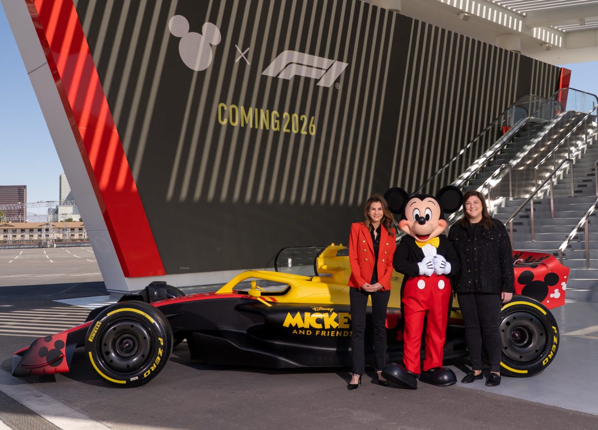 Formula 1 car with Mickey Mouse and team members at stadium backdrop