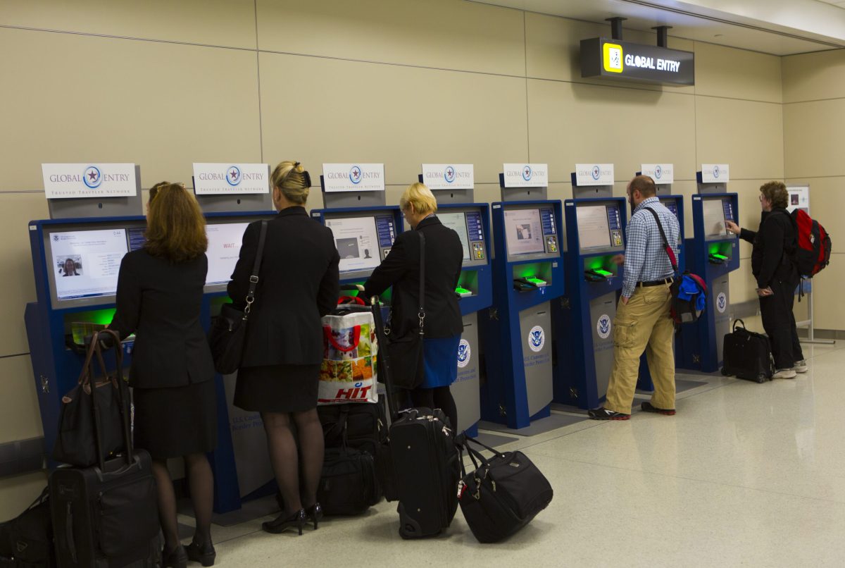 Travelers line up at automated passport control kiosks in an airport terminal