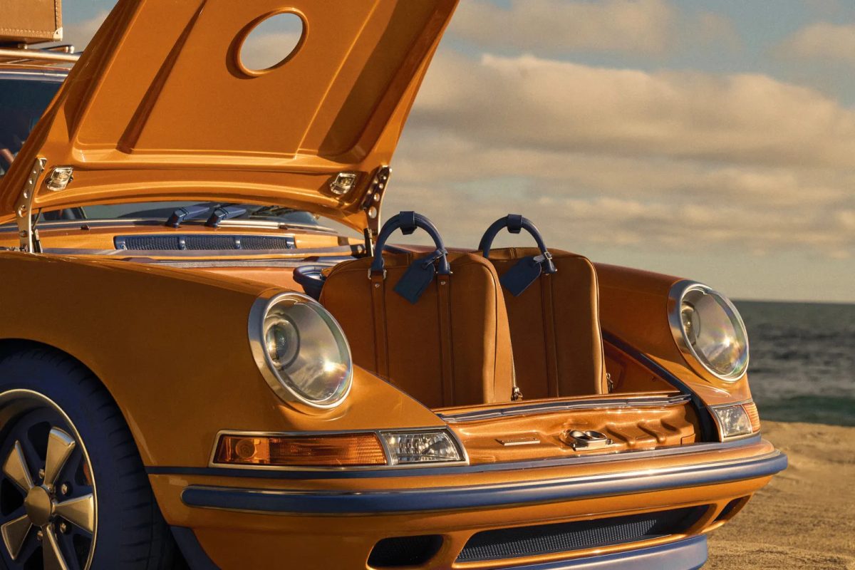 Gold Porsche 911 with open hood displaying brown Louis Vuitton luggage on beach