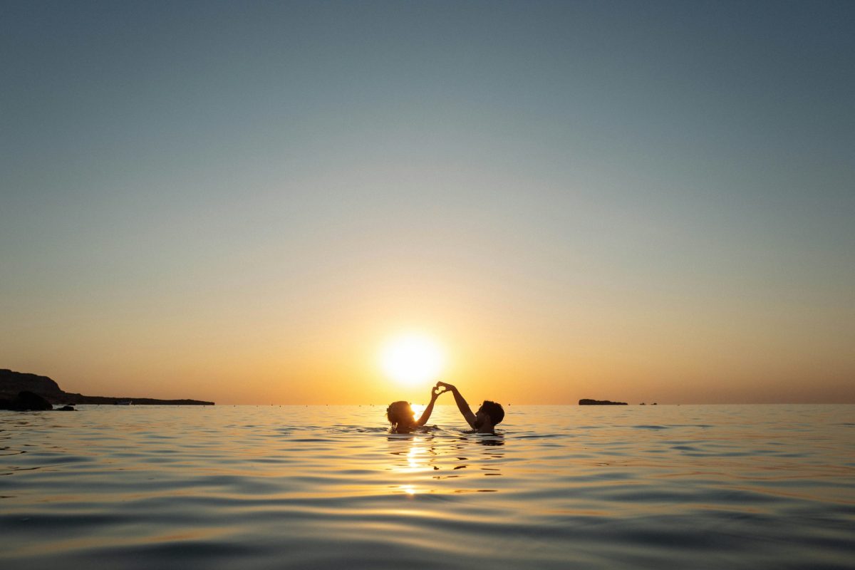 Silhouetted couple embracing in shallow water at sunset on a Greek island.