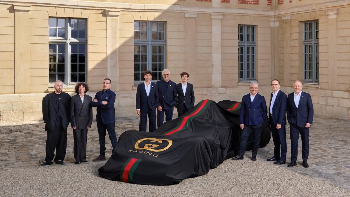 Group of executives standing beside a covered race car at a palatial venue