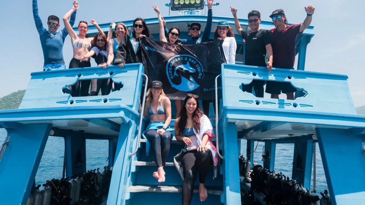 Group of tourists on a blue boat raising their arms in celebration after a dive
