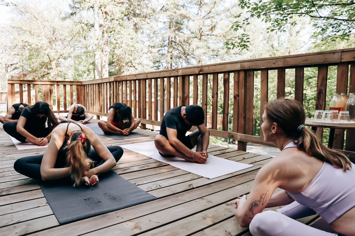 Group yoga class on wooden deck surrounded by autumn forest at eco-village retreat