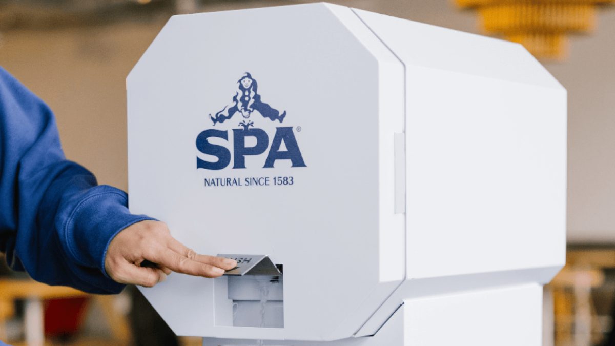 Hand touching a white SPA dispenser with the iconic SPA logo and 'Natural Since 1583' text