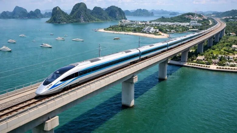 High-speed train crossing an elevated bridge over turquoise waters near limestone karsts