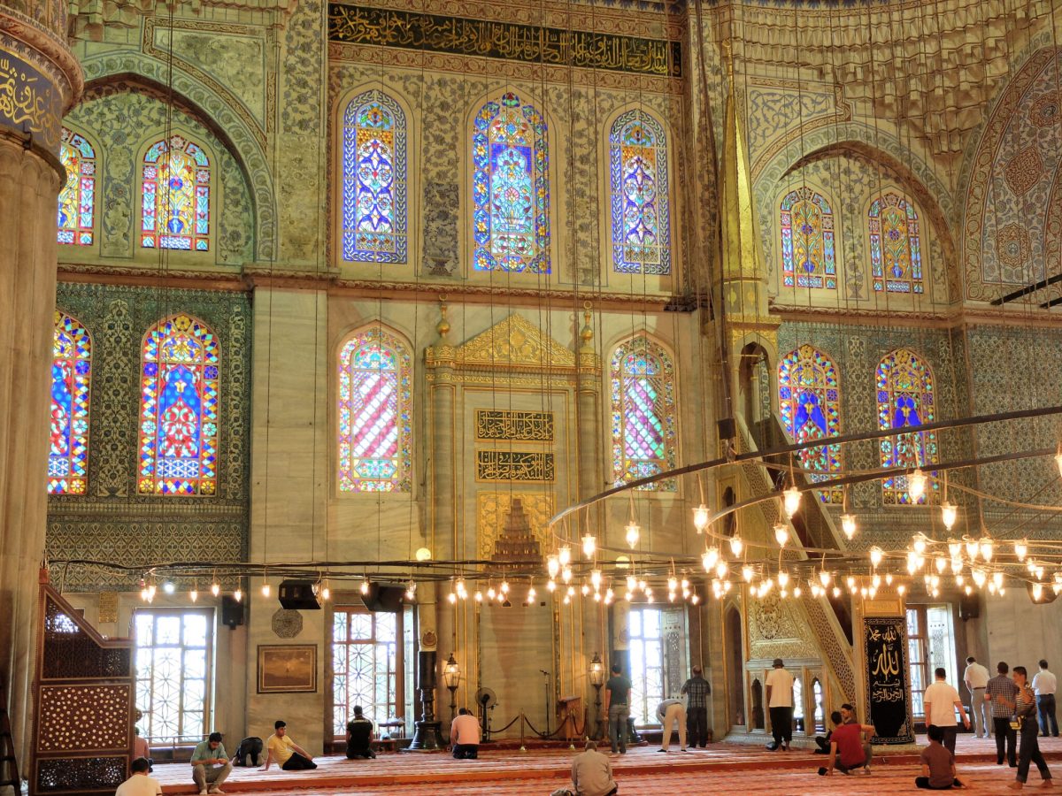 Interior of Blue Mosque showing stained glass windows, ornate tilework, and hanging chandeliers