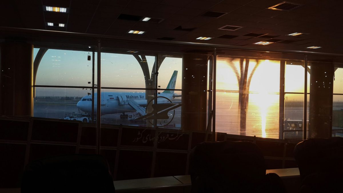 Airplane silhouetted against a sunset viewed from an airport terminal window.