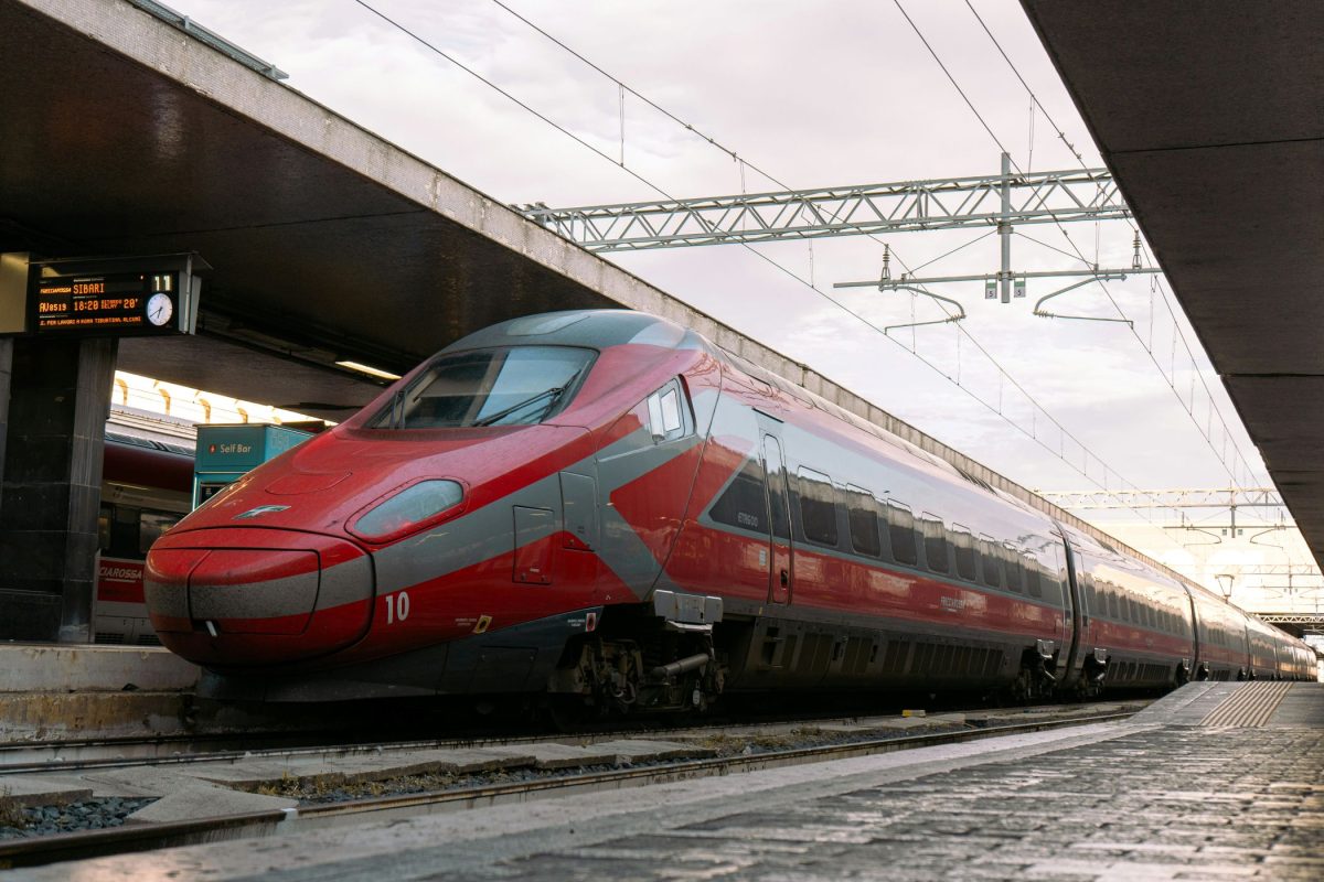 Red high-speed train at a covered station platform with overhead electrical lines