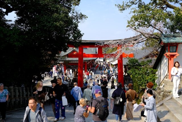 Crowds of tourists walking through a bright red torii gate at a Japanese temple shrine