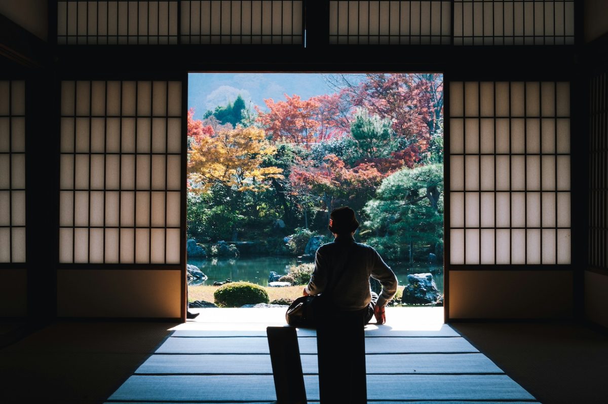 Person in traditional Japanese temple viewing blooming garden and water landscape