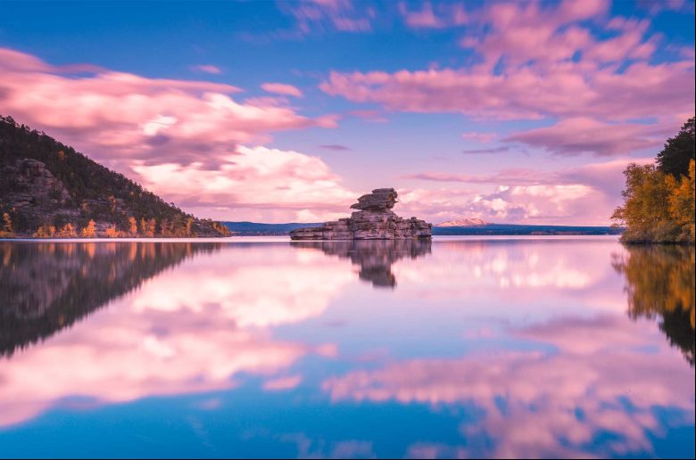 Lake Kaindy in Kazakhstan, reflecting colorful sky and rock formations.