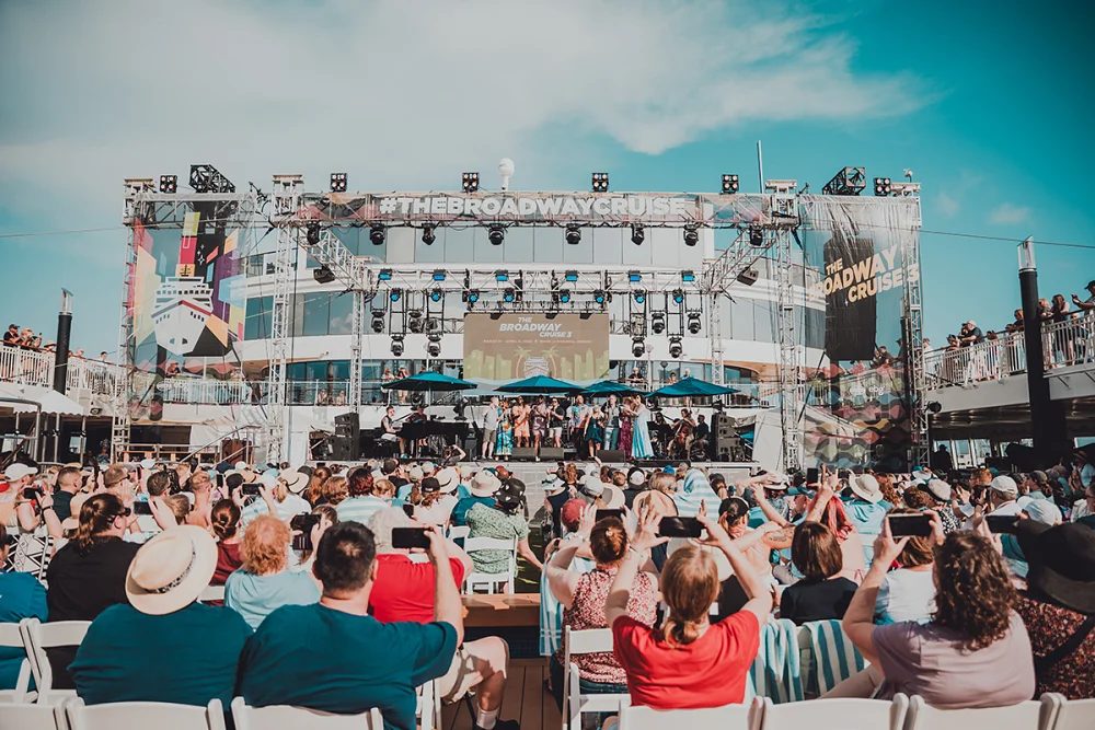 Large crowd enjoying a Broadway-themed cruise with stage and performers visible