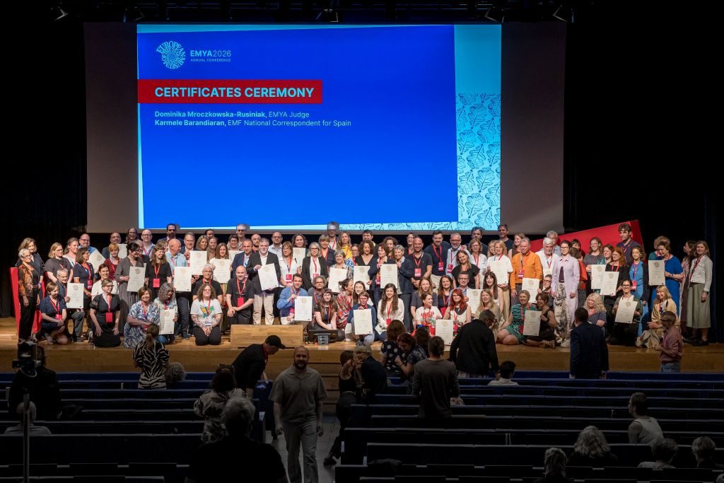 Large group of people on stage holding certificates at a museum award ceremony