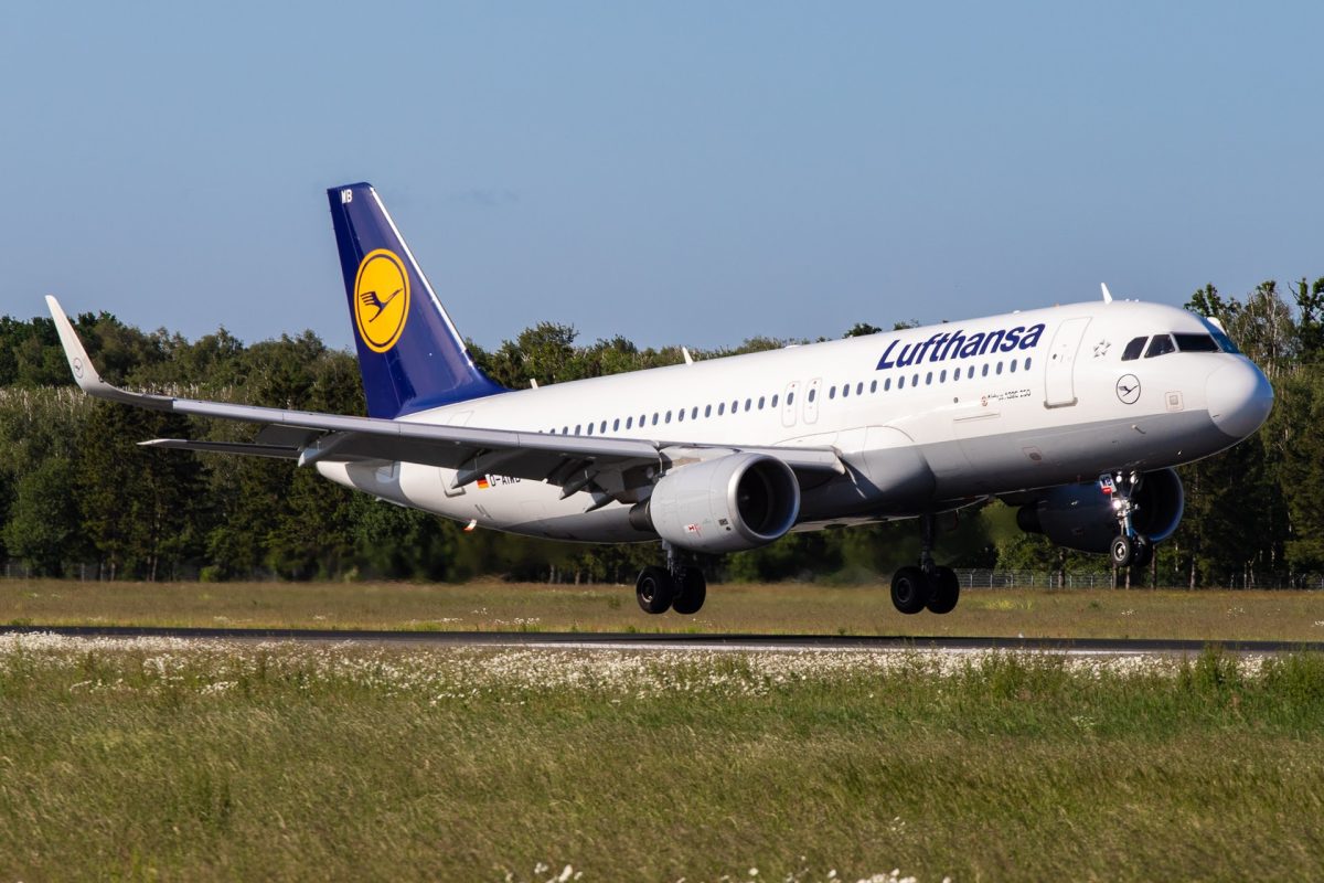 Lufthansa Airbus A320 aircraft landing on runway with green grass field