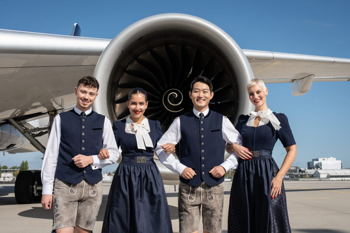 Lufthansa crew members in Bavarian-inspired uniforms pose in front of an airplane engine.