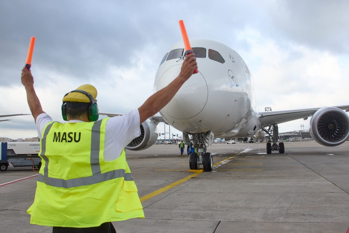 Ground crew member in yellow safety vest directing aircraft at airport tarmac
