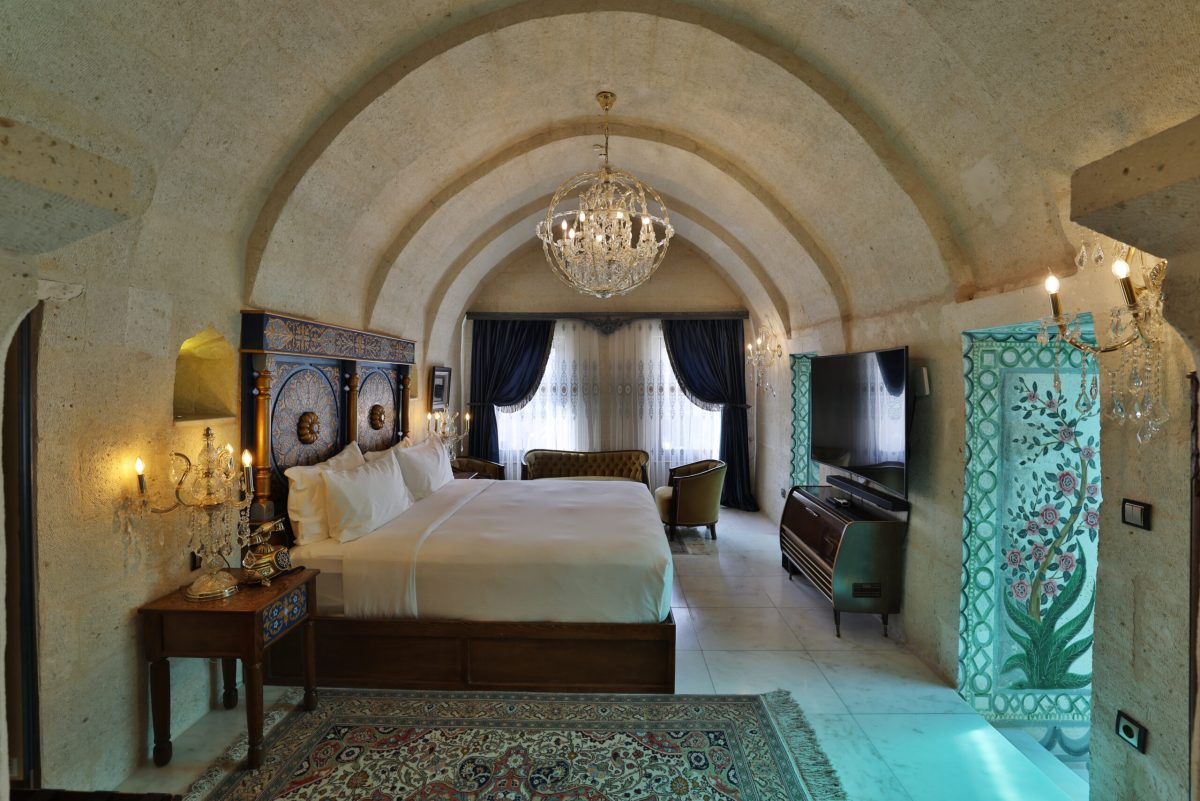 Luxurious cave hotel bedroom with arched ceiling, chandelier, and modern amenities in Cappadocia