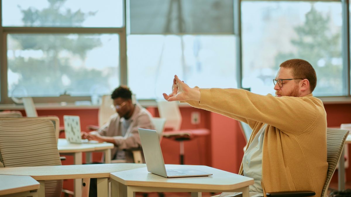 Man in yellow shirt stretching arms in airport lounge during travel