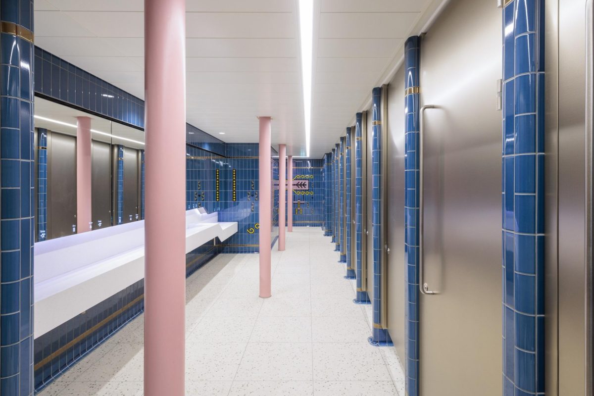 Modern bathroom with blue tiled walls, pink columns, and sleek white fixtures at Piccadilly Circus station