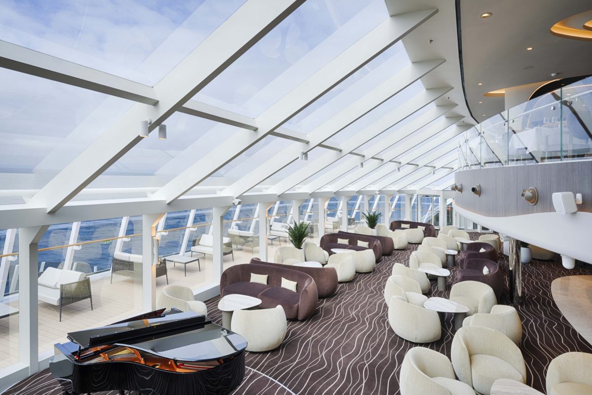 Modern cruise ship lounge with floor-to-ceiling windows overlooking the ocean and comfortable seating