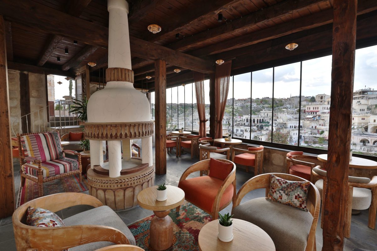 Modern lounge inside a cave hotel suite with wooden beams and panoramic windows overlooking Cappadocia