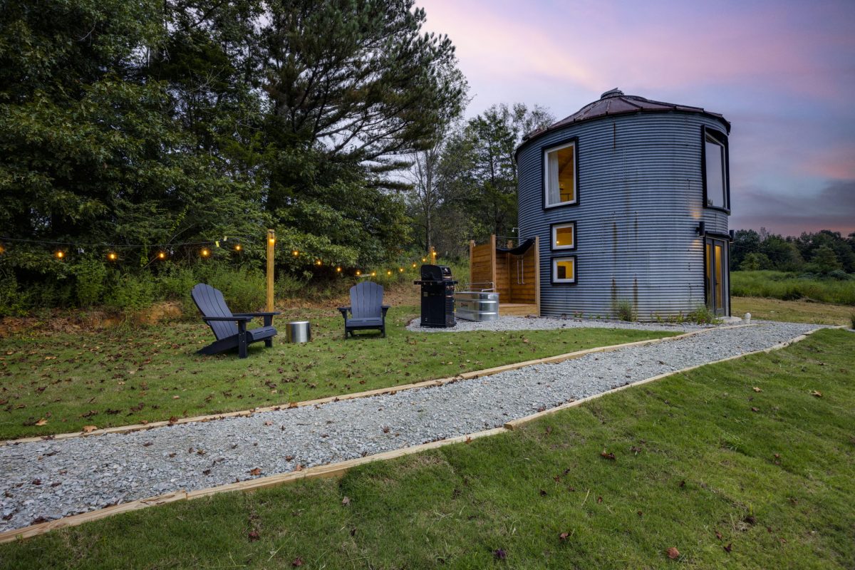 Modern tiny home with blue siding on grassy landscape at dusk with Adirondack chairs