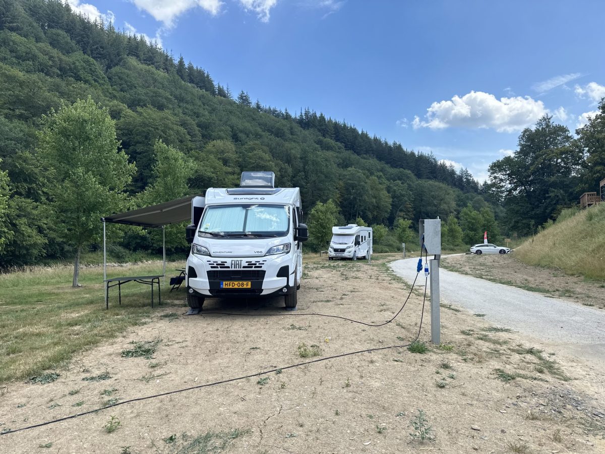 Motorhome parked at campsite with forested Ardennes hills in background