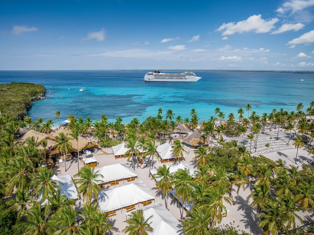 Aerial view of tropical beach resort with cruise ship anchored offshore in turquoise waters