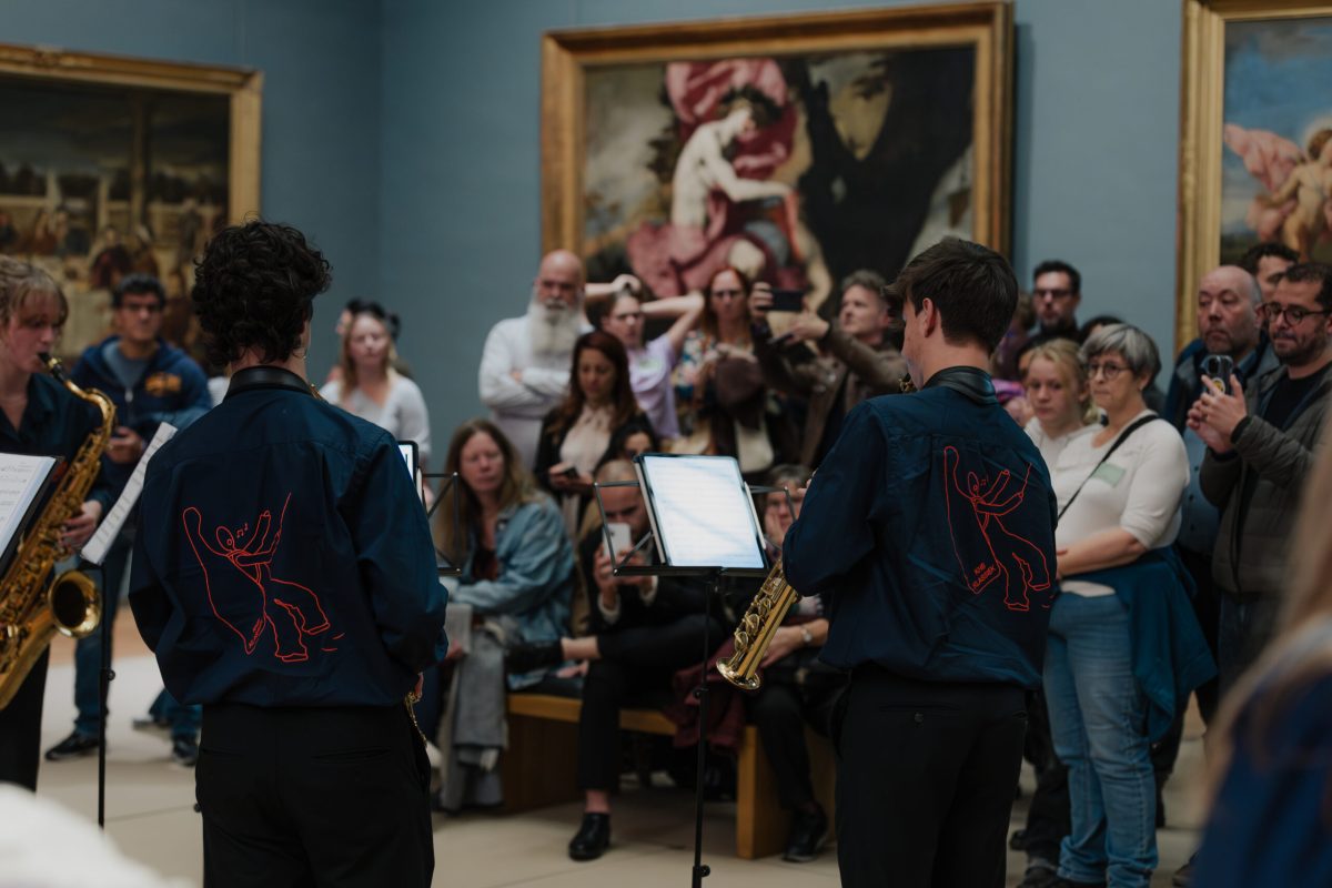 Museum visitors listen to a saxophone quartet performing amidst artwork.