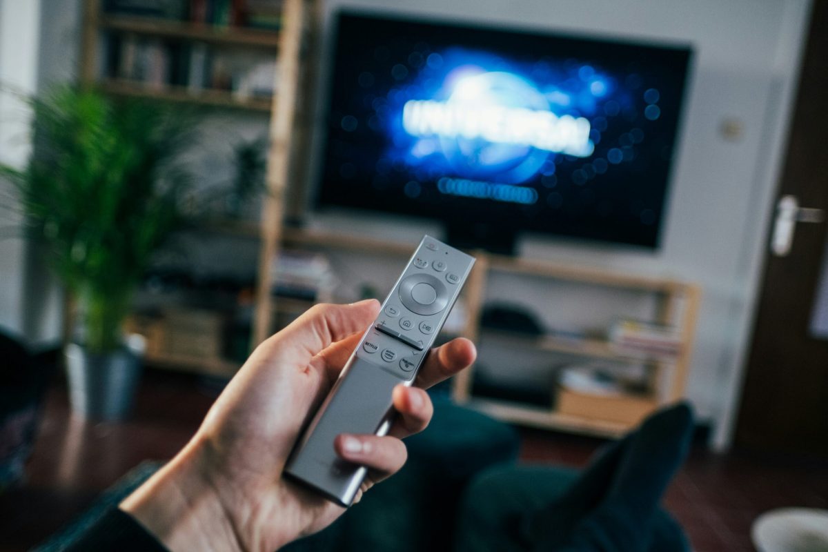 Hand holding remote control pointed at TV displaying scenic cloud landscape
