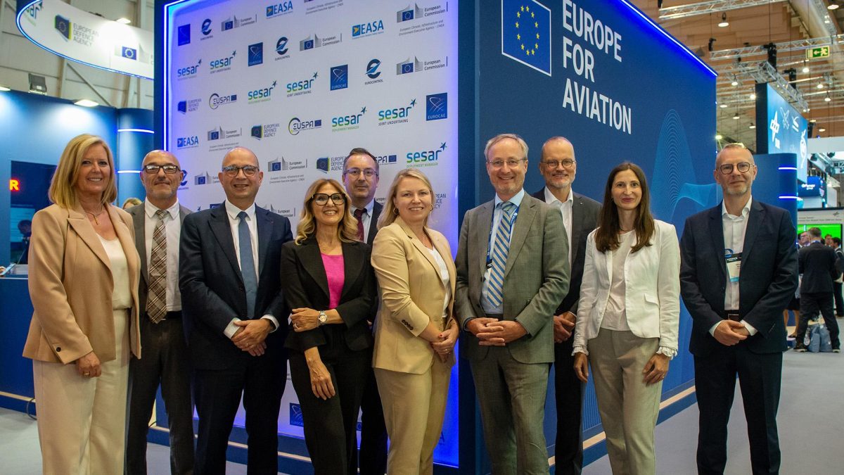 Nine government officials and aviation leaders stand before a blue 'Europe for Aviation' conference backdrop
