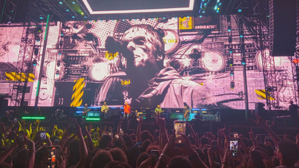 Crowd at a concert, illuminated by a large screen displaying a band member's face.