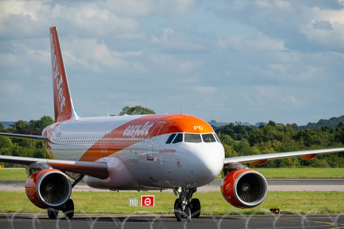 Orange and white aircraft on runway with green field and trees in background