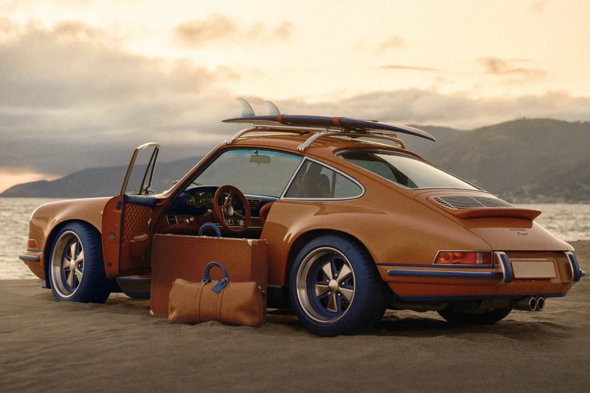 Orange Porsche 911 with open door displaying Louis Vuitton luggage and accessories on beach