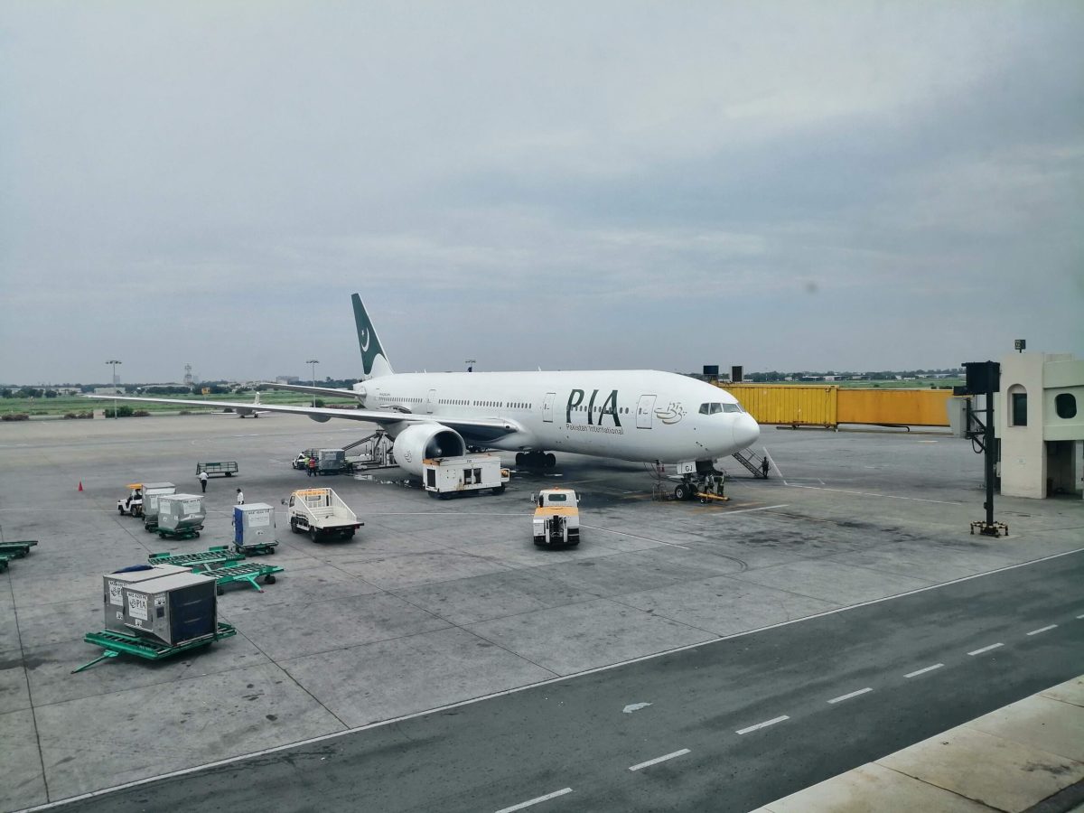 PIA aircraft parked at airport gate with ground support vehicles