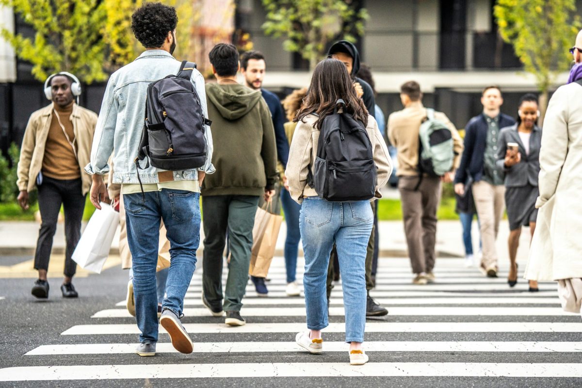 Pedestrians crossing a zebra crossing in an urban area, some wearing backpacks