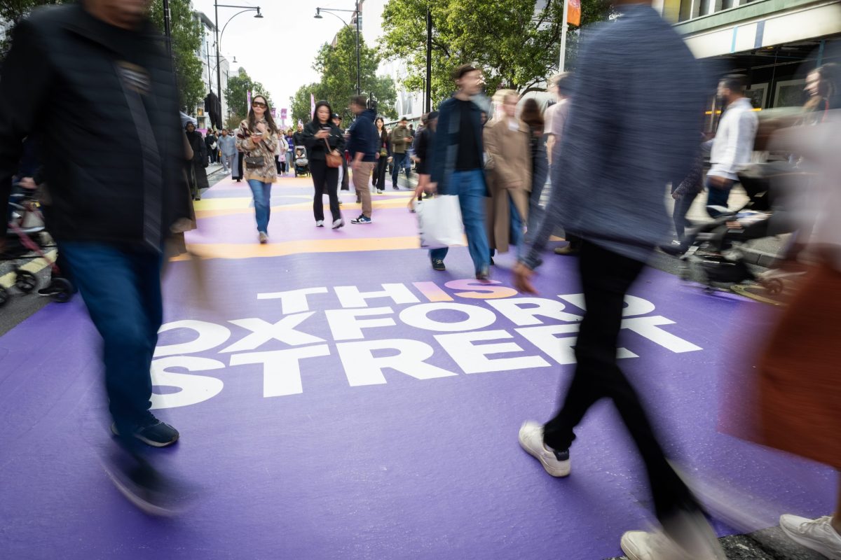 Pedestrians walk across a vibrant purple crosswalk on Oxford Street, London.