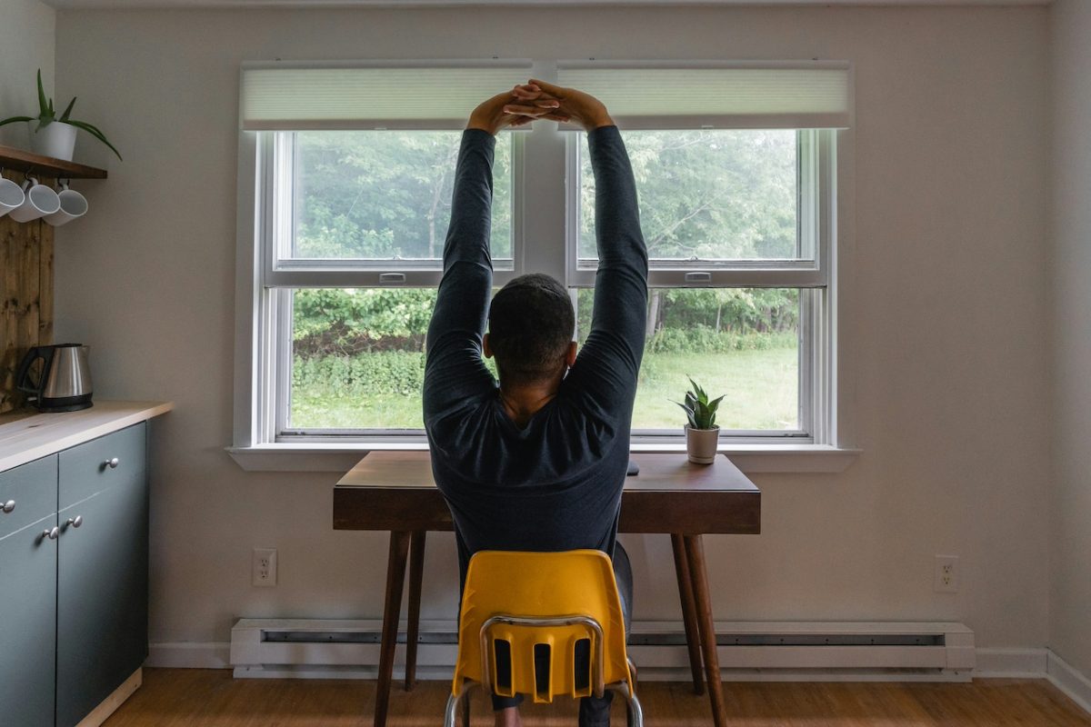 Person performing overhead stretch exercise on yellow stool at home