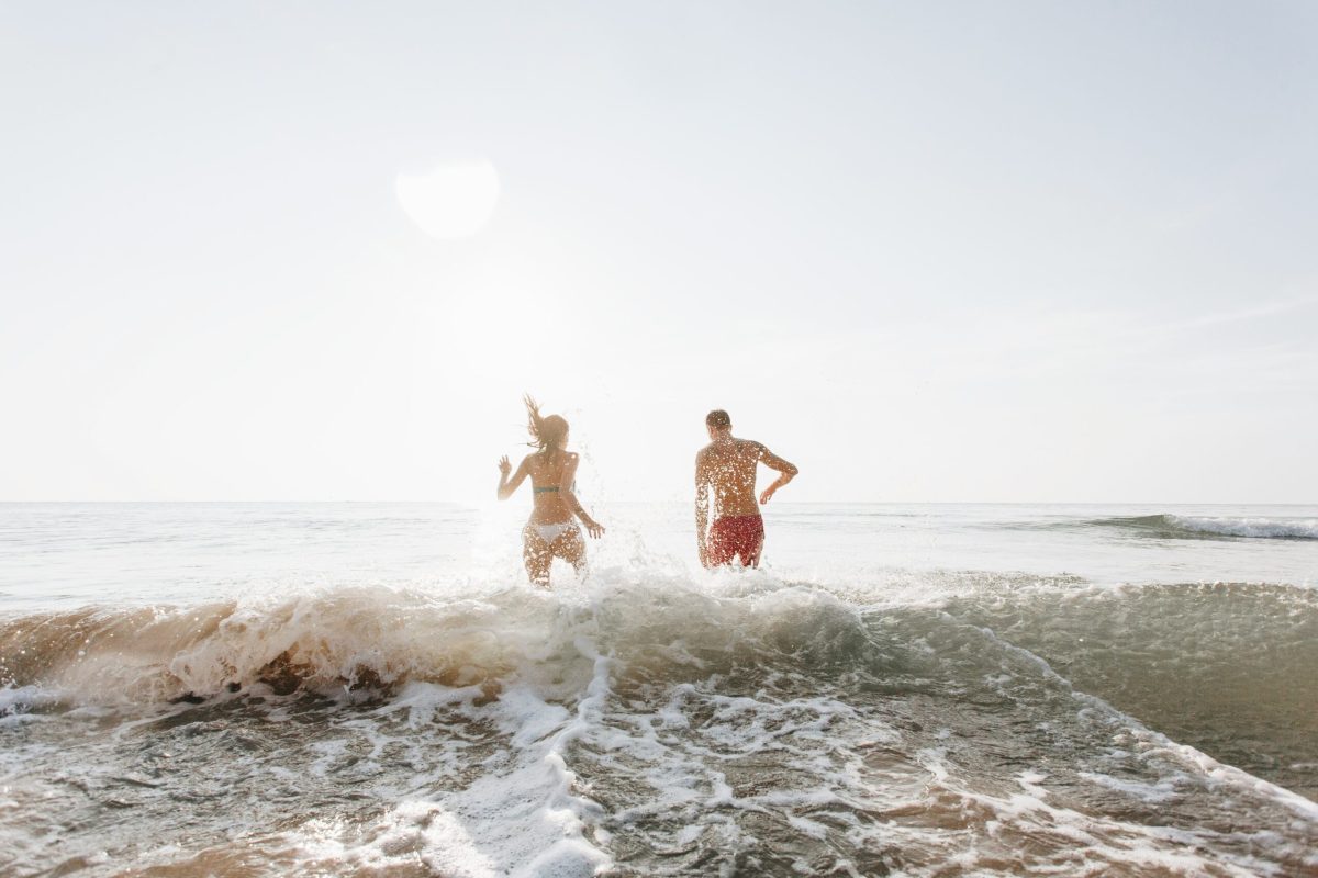 Two people running into turquoise waves on a pristine beach with pink sand