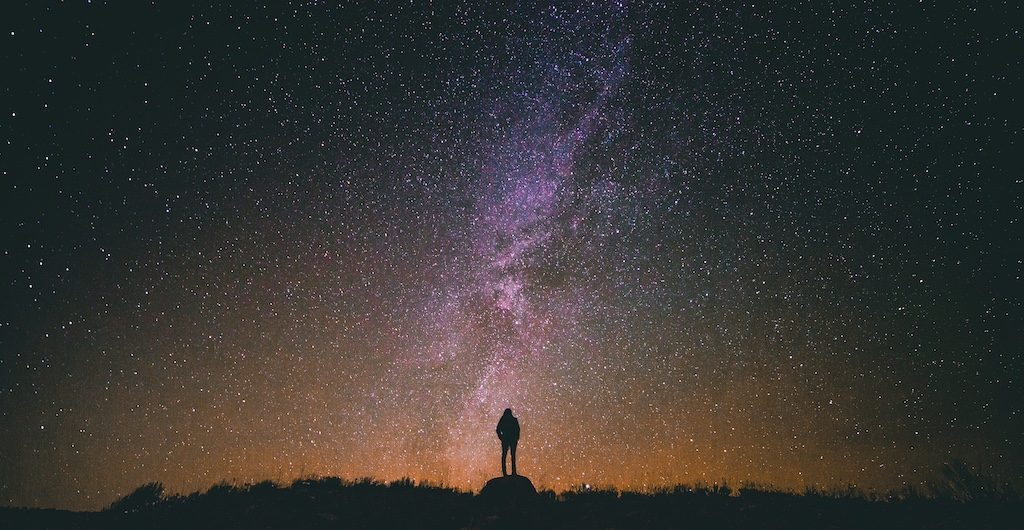 Silhouette of person standing under Milky Way galaxy at night