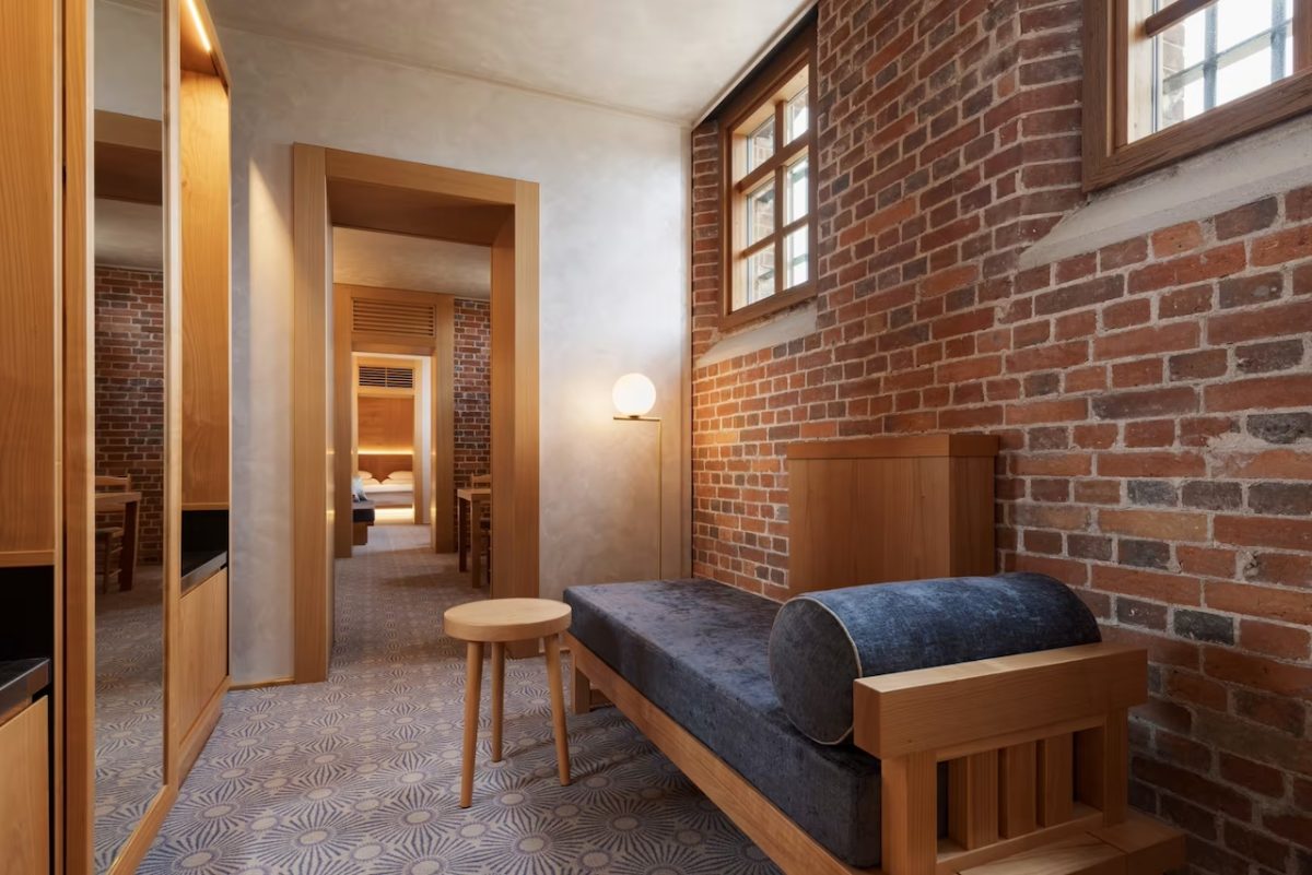 Prison-themed hotel room with brick walls, wooden bed frame, and minimalist furnishings