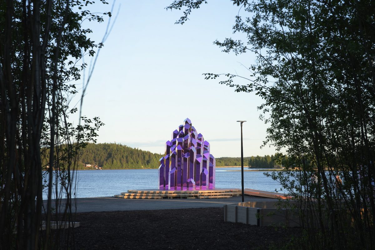 Purple crystal-shaped sauna structure on a dock by a lake surrounded by forest