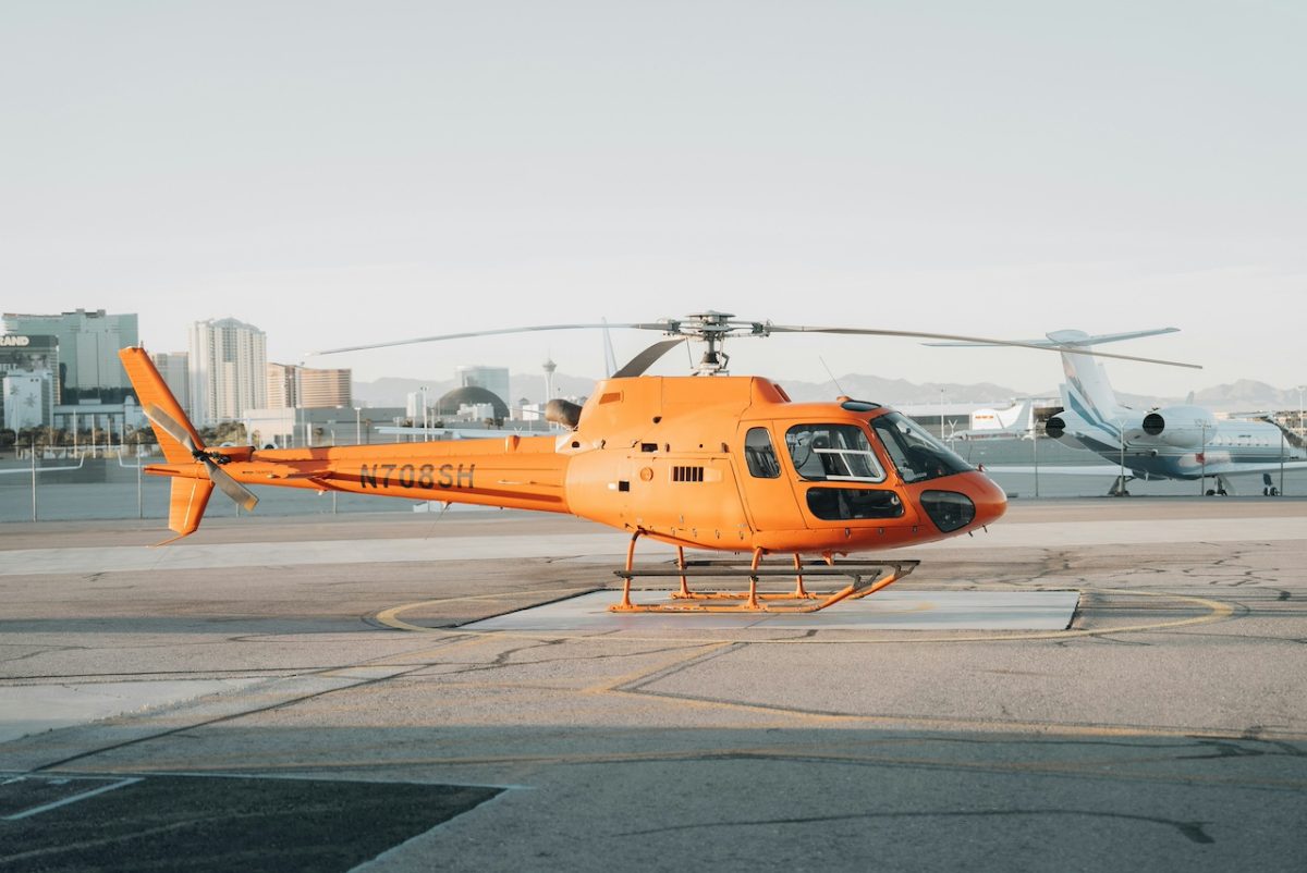 Orange helicopter parked on airport tarmac with city skyline in background