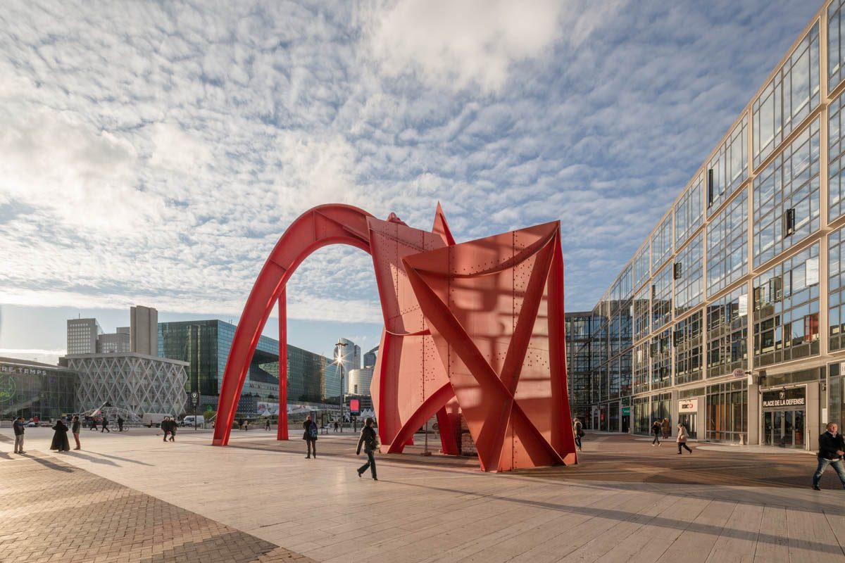 Red modern sculpture in a contemporary Paris plaza with buildings and blue sky