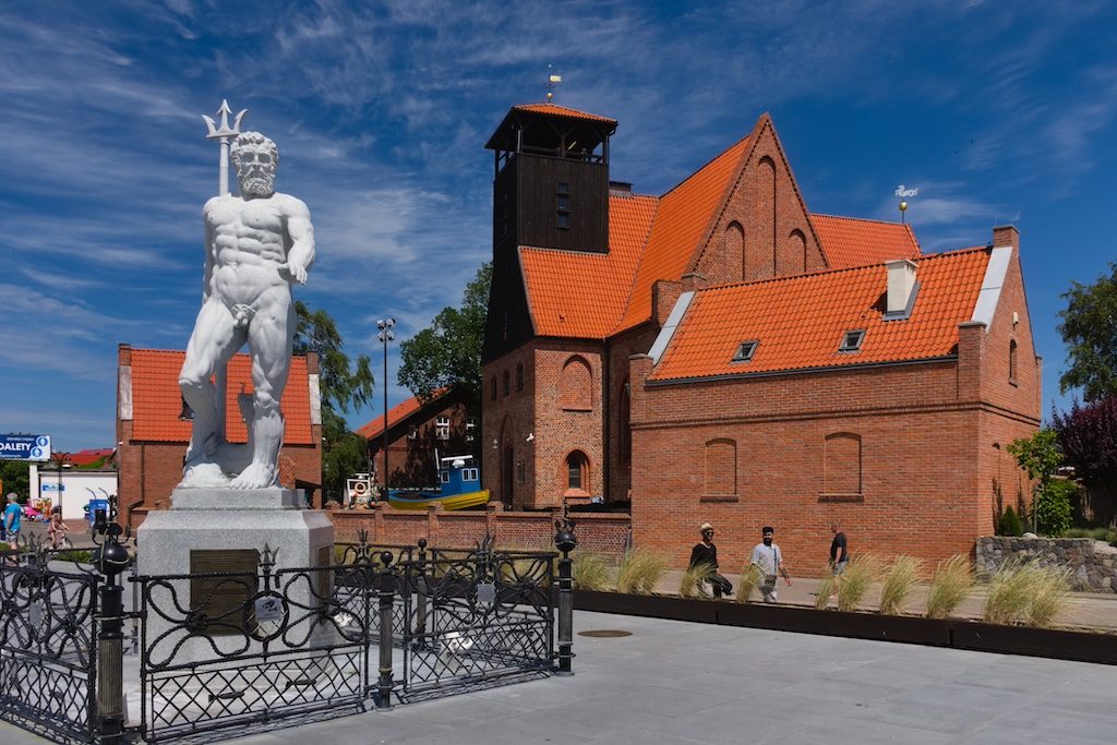 Red-roofed brick church with white statue and tower in Polish coastal town