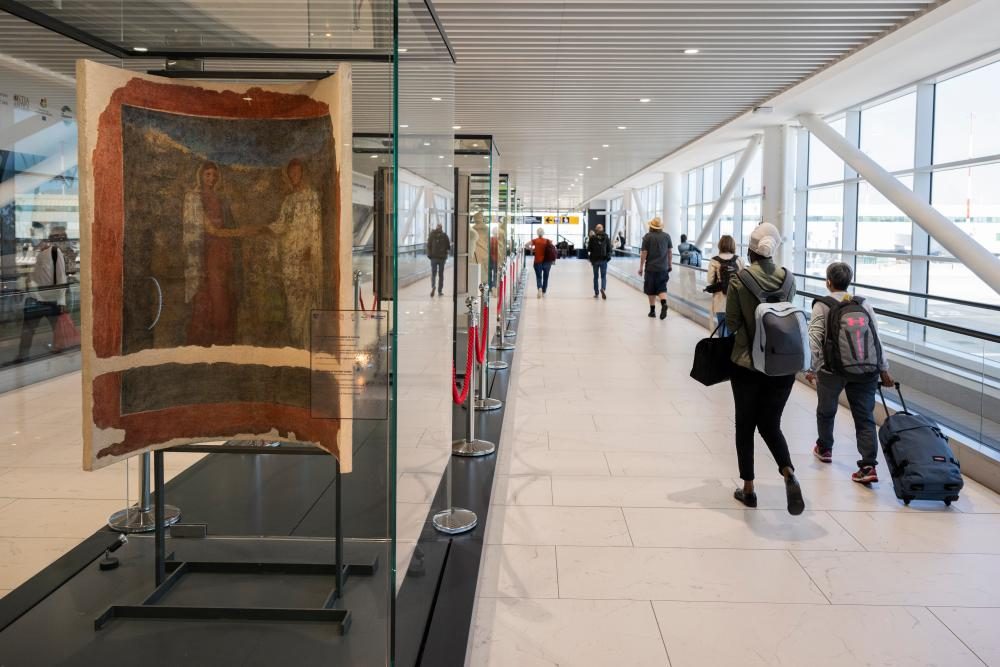 Airport terminal with travelers walking past artwork display near security checkpoint