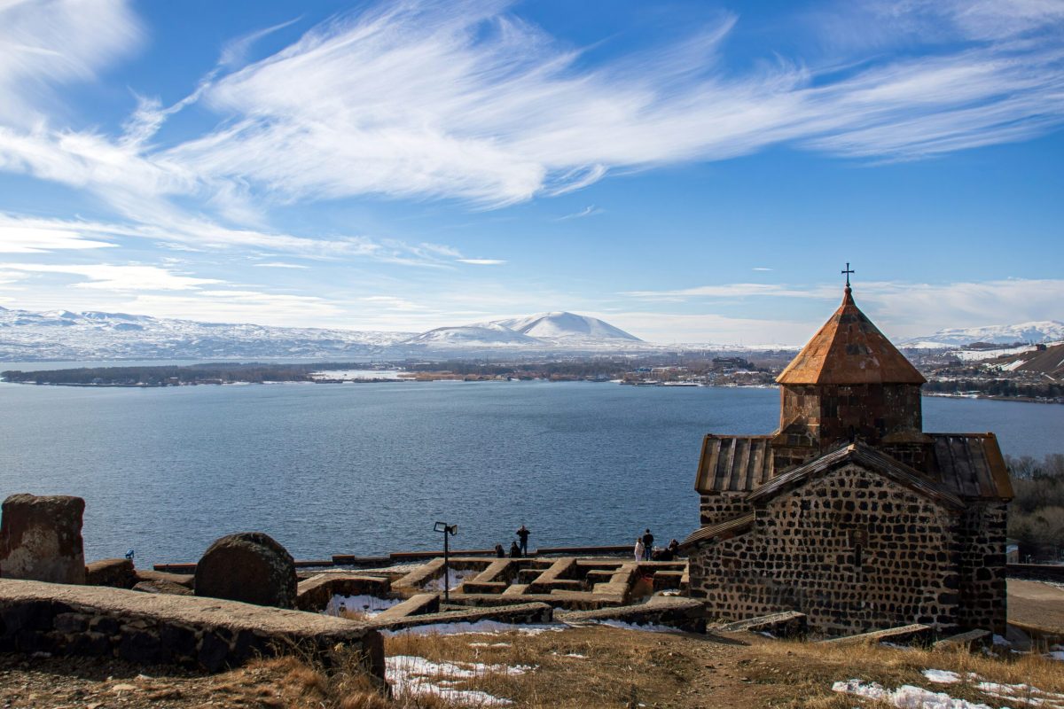 Sevan Monastery on rocky peninsula overlooking Lake Sevan with snow-capped mountains